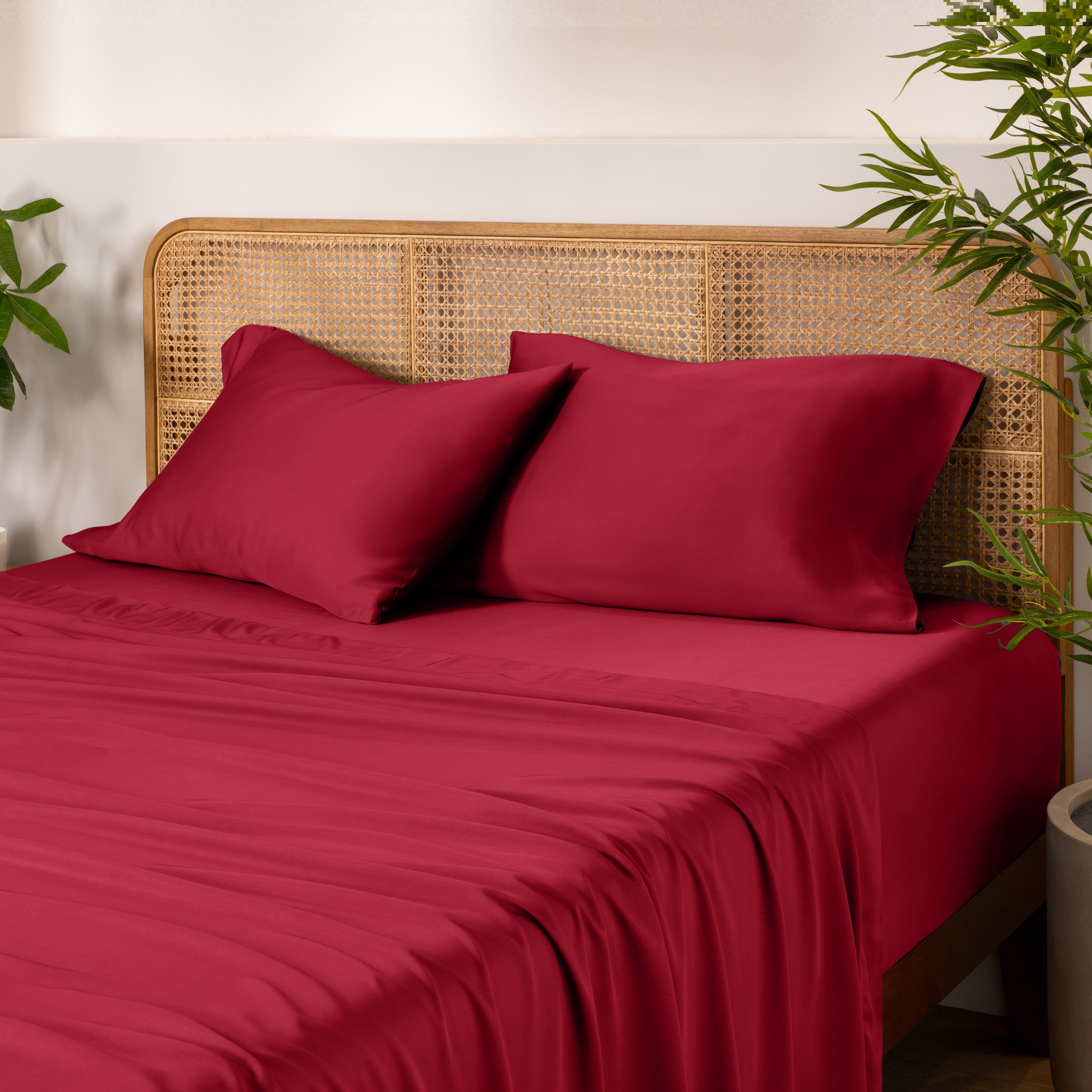 Bamboo bed sheets and pillows on a bed with a wicker headboard and plants in the background.