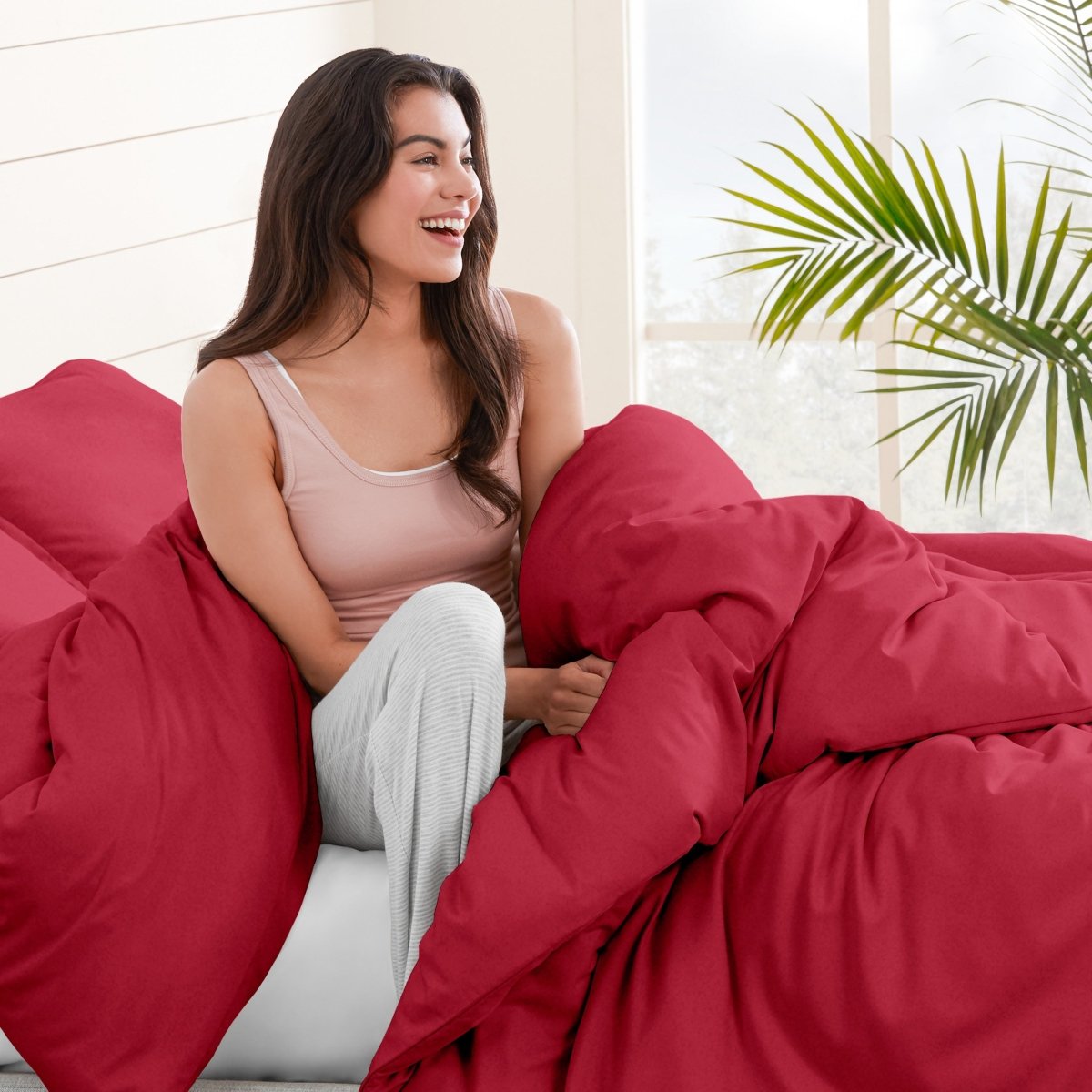 Woman sitting on a bed under duvet cover with a plant in the background