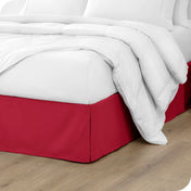 A modern bed with a microfiber bed skirt with pleats on the corners and midway on each side.