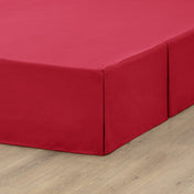 The corner of a box spring with a pleated bed skirt on it
