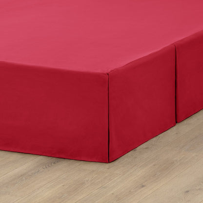 The corner of a box spring with a pleated bed skirt on it