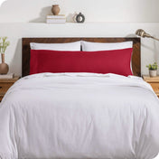 A body pillow cover on a pillow on a bed with other pillows and a duvet cover