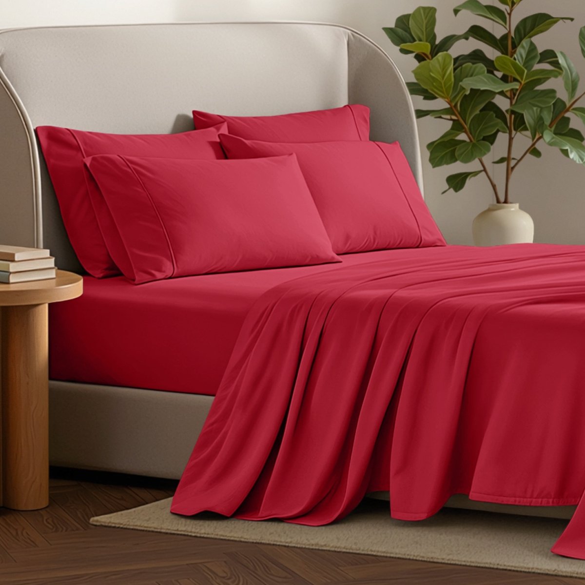 Bed sheets and pillows on a bed with a plant and side table in the background.