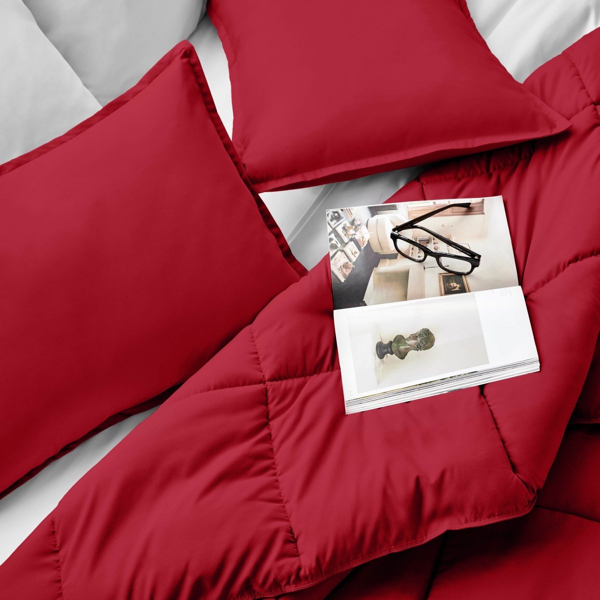 Comforter and pillows on a bed with a magazine and glasses.