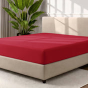 A fitted sheet covering a bed with a cream colored frame, styled in a bedroom setting with a large potted plant.