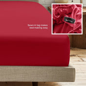A fitted bed sheet on a bed frame with a small inset close-up of the elastic and a sewn-in tag labeled BOTTOM. White text on the sheet reads, 'Sewn-in tag makes bed-making easy.