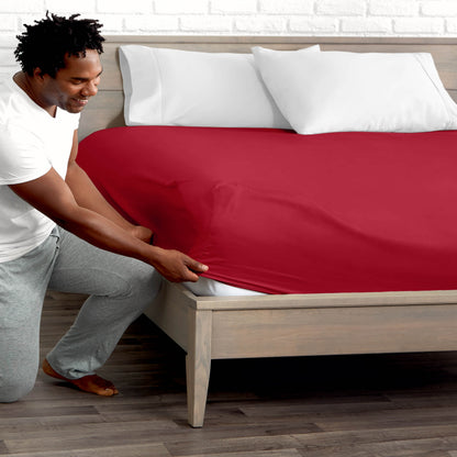 Man adjusting fitted sheet on a bed with white pillows.