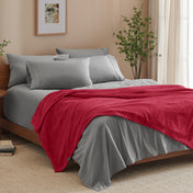 A bed made with grey sheets and a microplush blanket