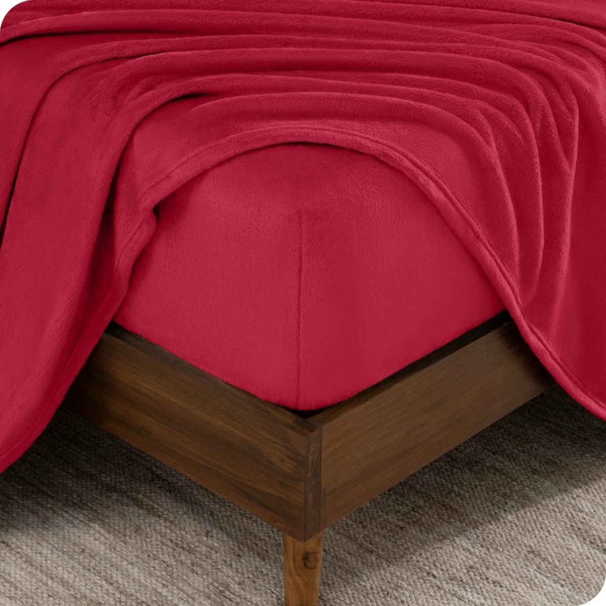 The corner of a bed frame and mattress with a fitted sheet and flat sheet on it.