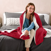 A woman sitting on a bed with a Sherpa blanket around her