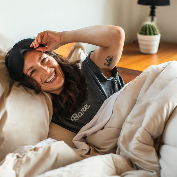 Woman laying in a bed with sand colored sheets and a Bare Home Shirt