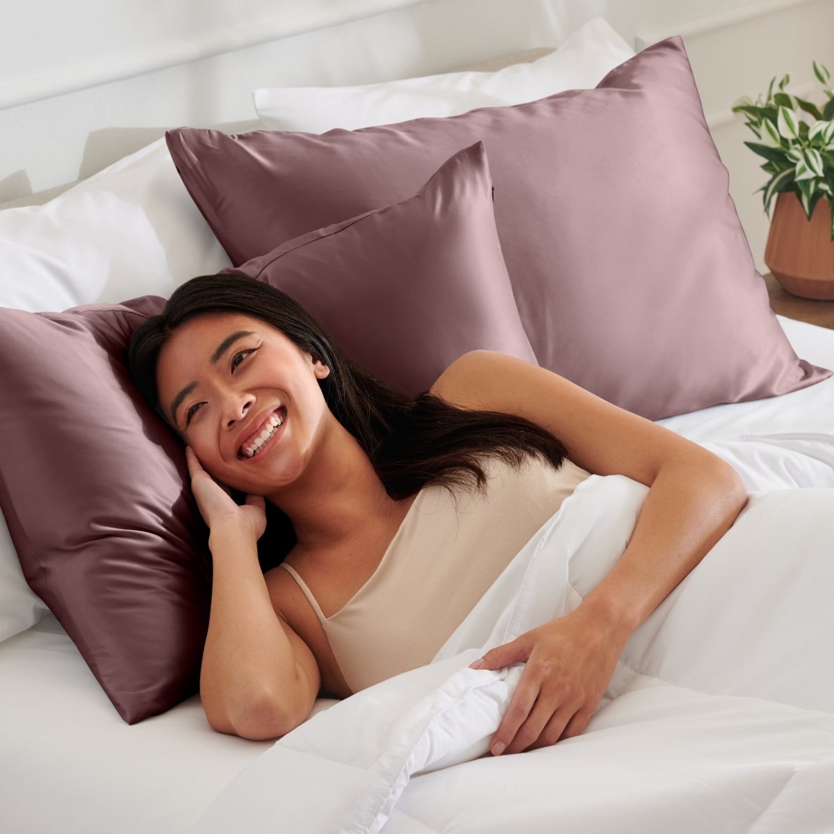 Woman lying on a bed with satin pillows and white bedding