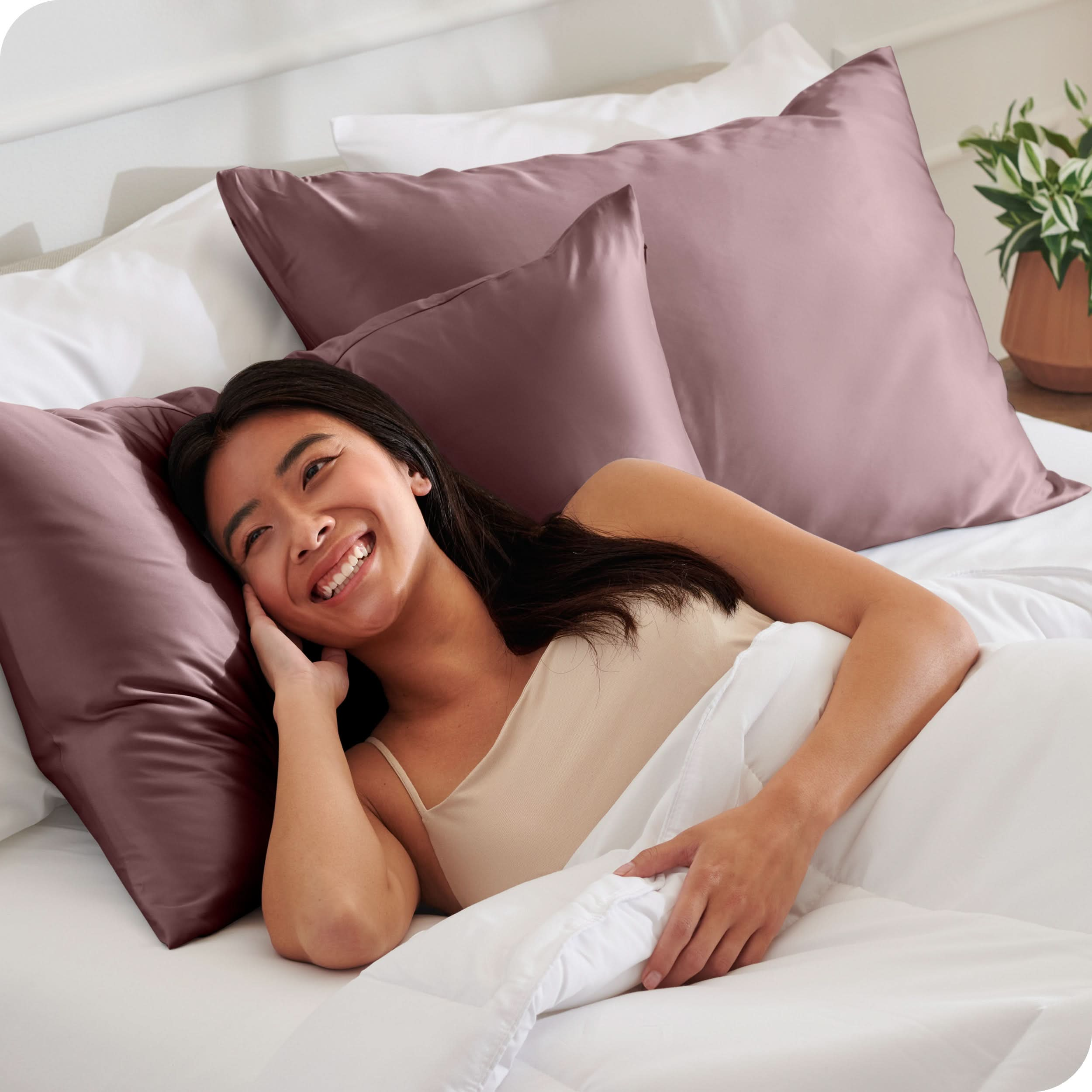 A woman is in bed and resting her head on a satin pillowcase