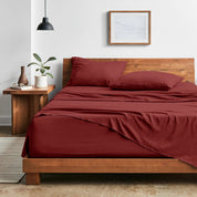 Bedroom with sheet set on a wooden bed frame, side table with plant and lamp.