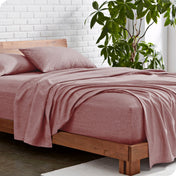 Bed with heather sheets and wooden frame against a white brick wall with a plant.