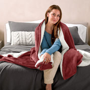 A woman sitting on a bed with a Sherpa blanket around her