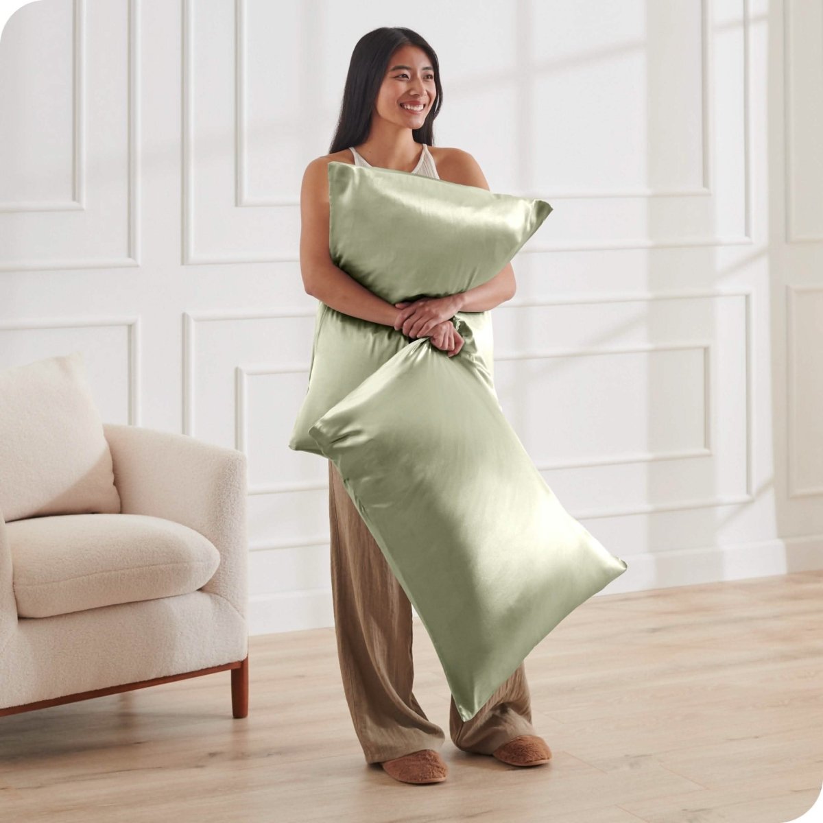 A woman standing while holding pillows with silk pillowcases on them