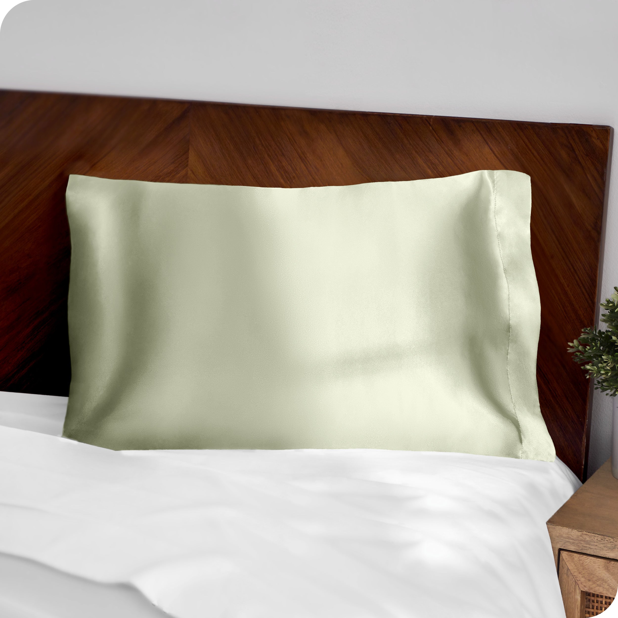 A green silk pillowcase on a pillow resting on a headboard
