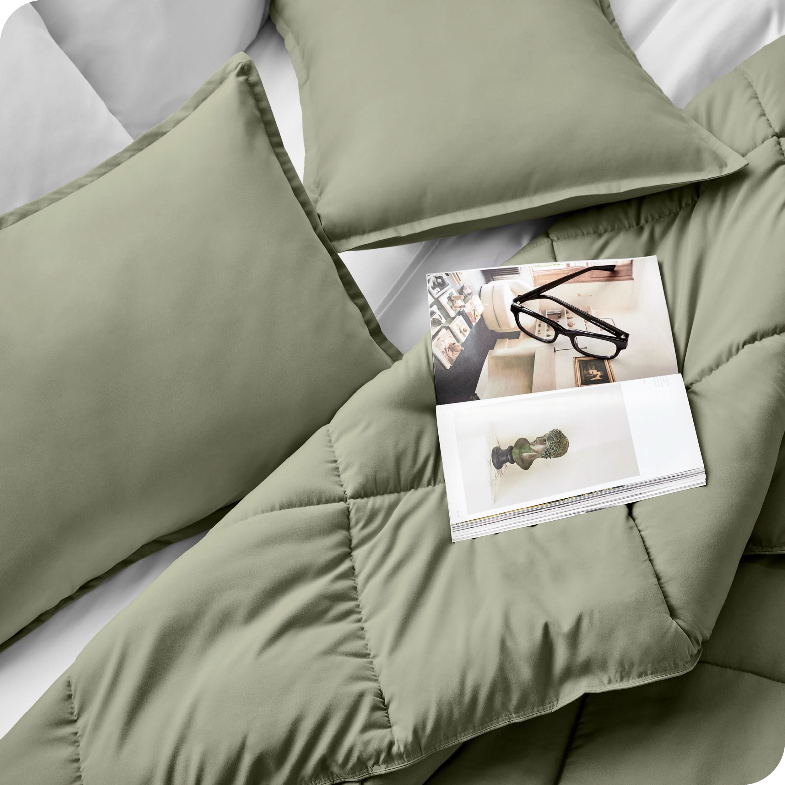 Close up of a comforter set on a bed. There are glasses and a magazine on top of the comforter.