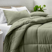 Comforter and pillow shams on a bed with a white brick wall and plant in the background