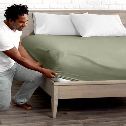 Man adjusting fitted sheet on a bed with white pillows.