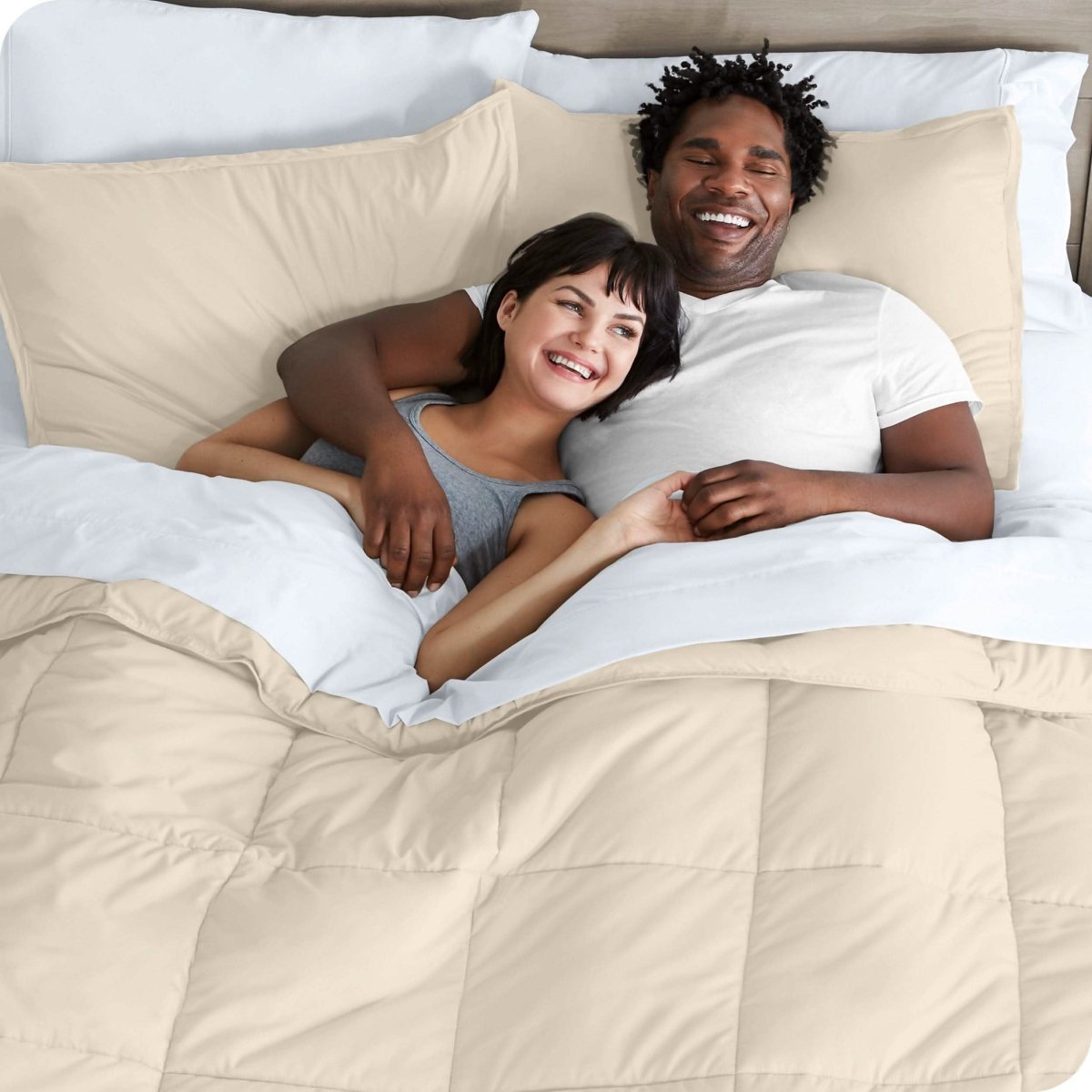 A couple is lying in bed with a comforter and sheets over them