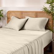 Bamboo bed sheets and pillows on a bed with a wicker headboard and plants in the background.