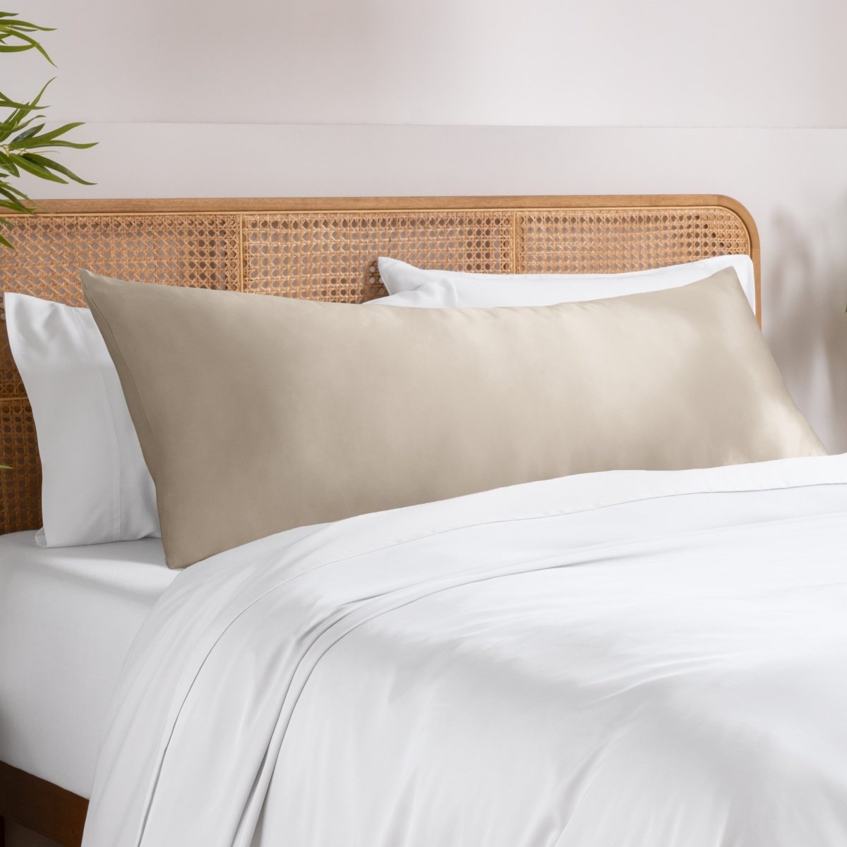 Body pillowcase on a pillow set on a bed with a wicker headboard and a plant in the corner.