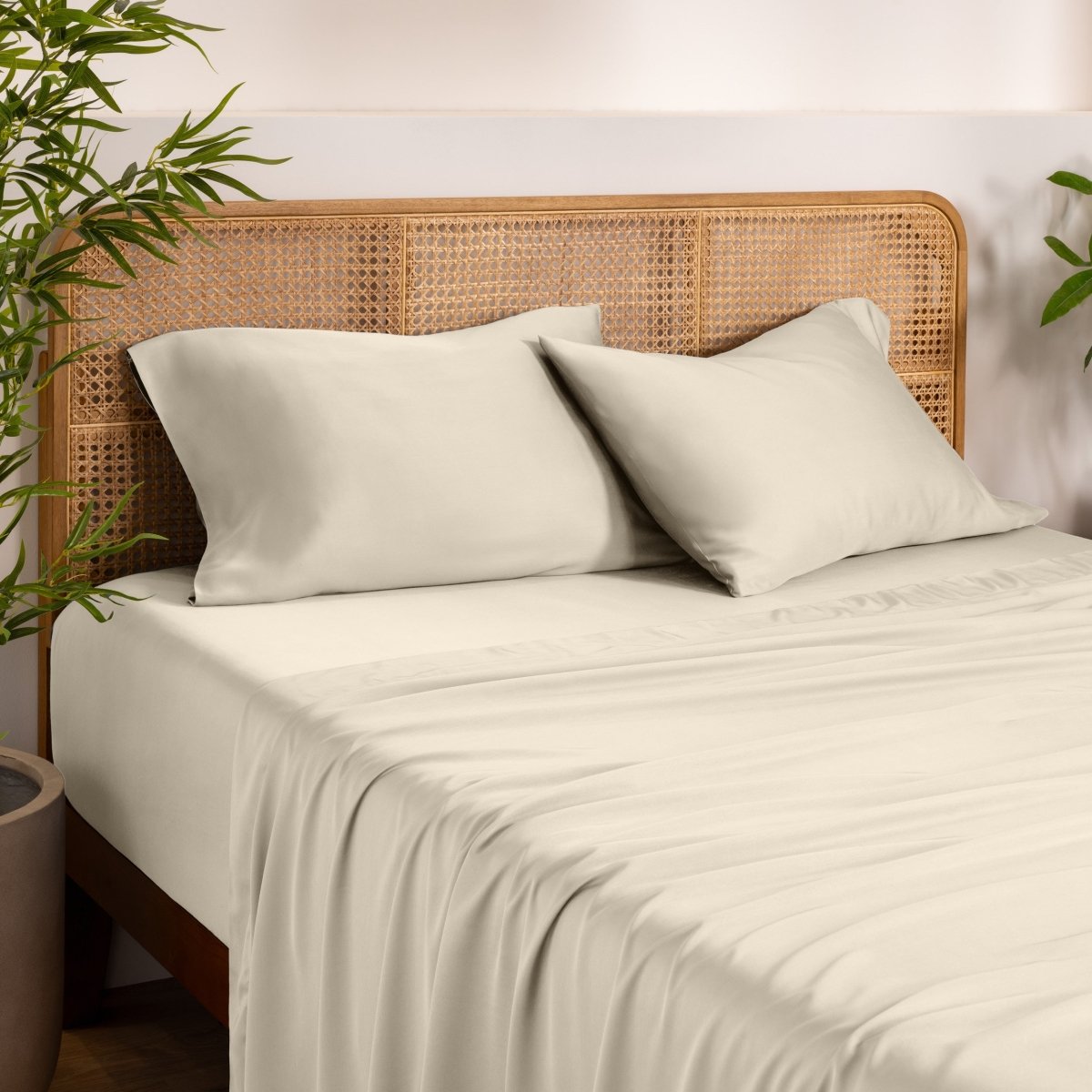 Bamboo bed sheets and pillows on a bed with a wicker headboard in a room with plants.