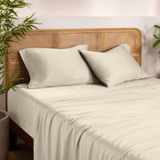 Bamboo bed sheets and pillows on a bed with a wicker headboard in a room with plants.