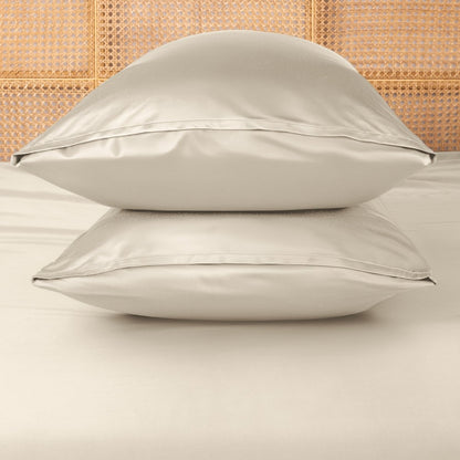 Two sand pillows stacked on a bed with a woven headboard.