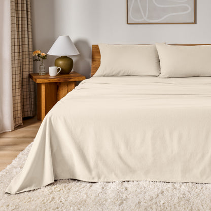 A bed dressed in flannel sheet set in a bedroom with a wooden headboard, bedside table and lamp