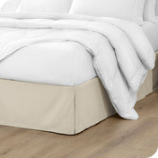 A modern bed with a microfiber bed skirt with pleats on the corners and midway on each side.