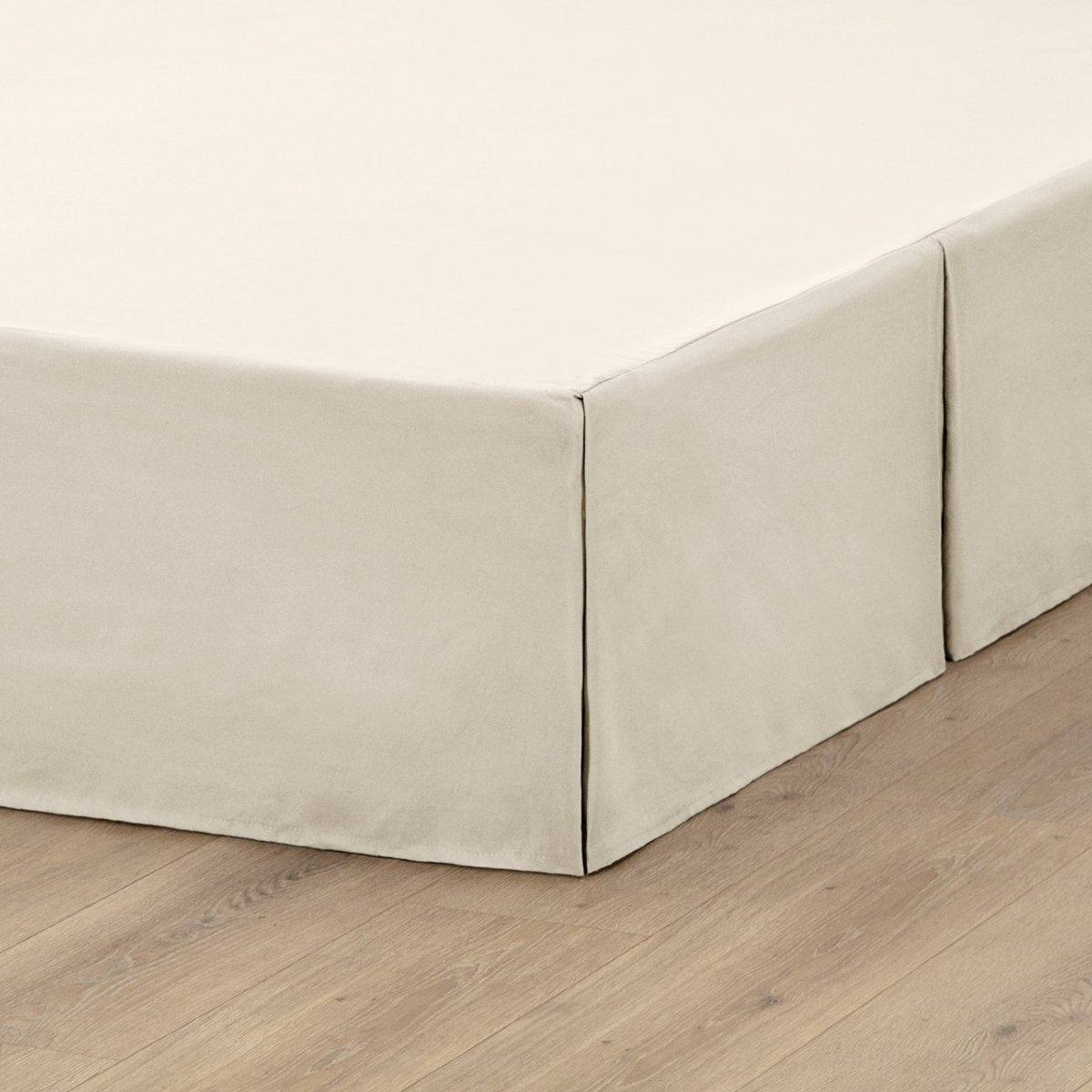 The corner of a box spring with a pleated bed skirt on it