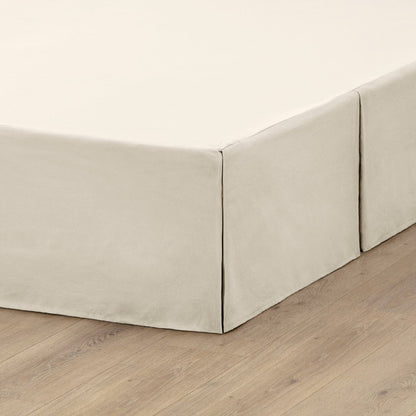 The corner of a box spring with a pleated bed skirt on it
