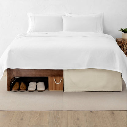One side of a bed has shoes and a box under it while the other side has a bed skirt so that under the bed is hidden from view