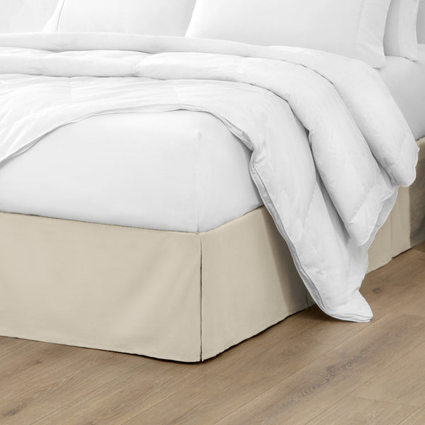 A modern bed with a microfiber bed skirt with pleats on the corners and midway on each side