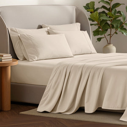 Bed sheets and pillows on a bed with a plant and side table in the background.