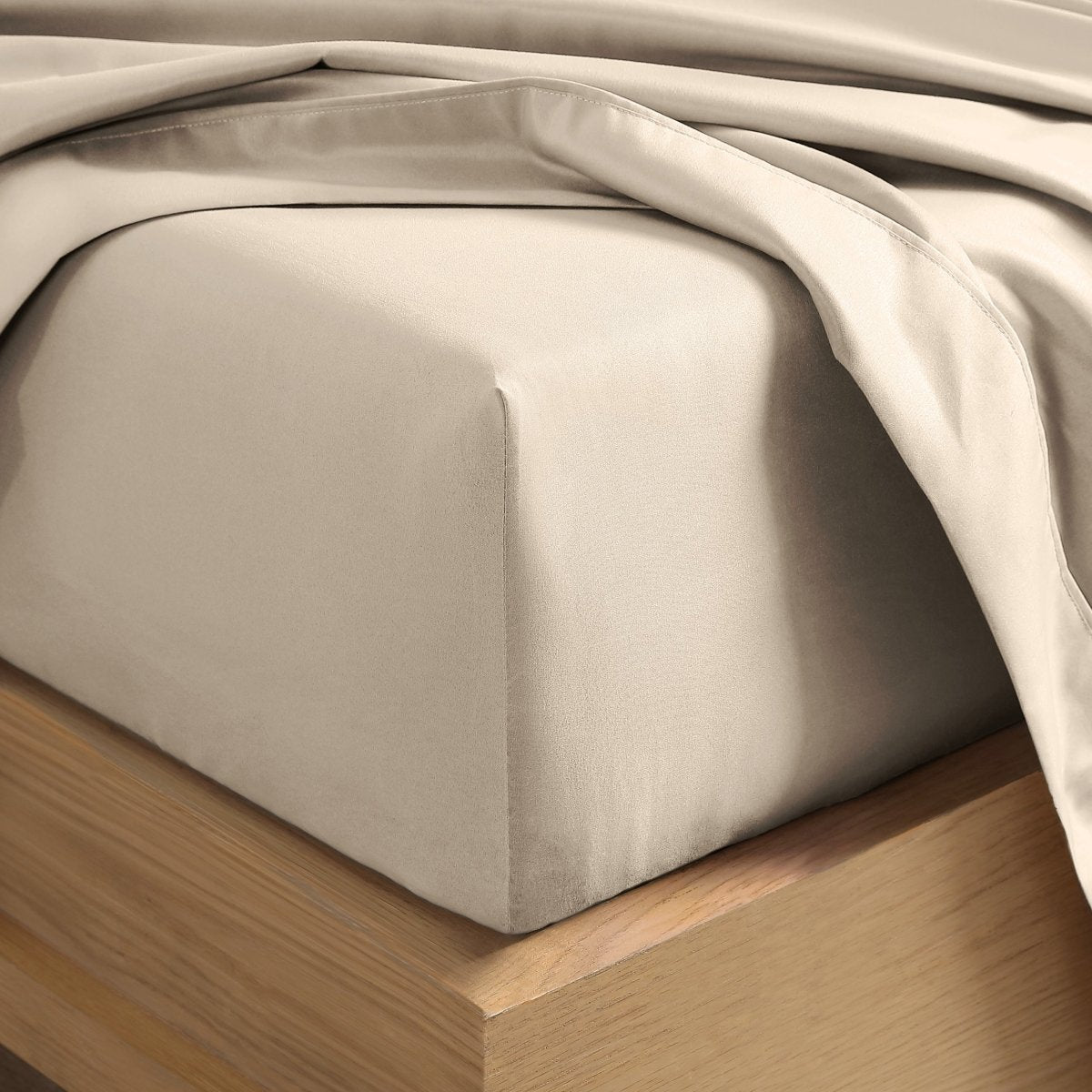 A close-up of a fitted sheet covering the corner of a bed frame, with matching top sheet draped over it.