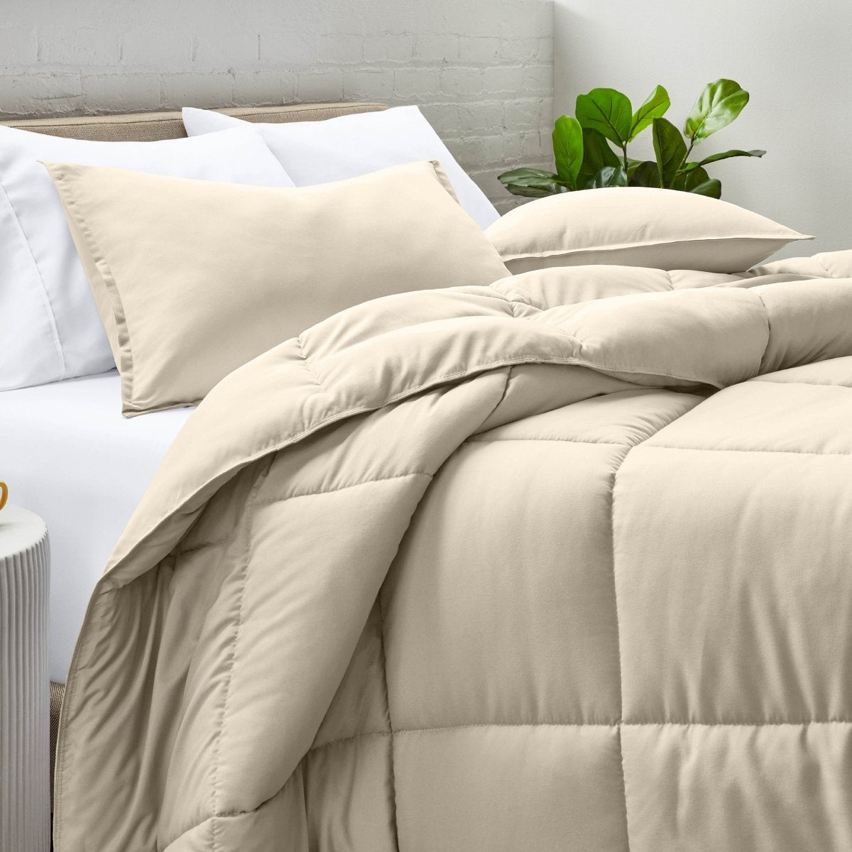 Comforter and pillow shams on a bed with a white brick wall and plant in the background