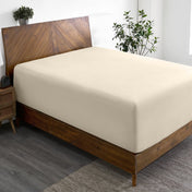 Wooden bed frame with a fitted sheet on the mattress in a room with plants and a nightstand.