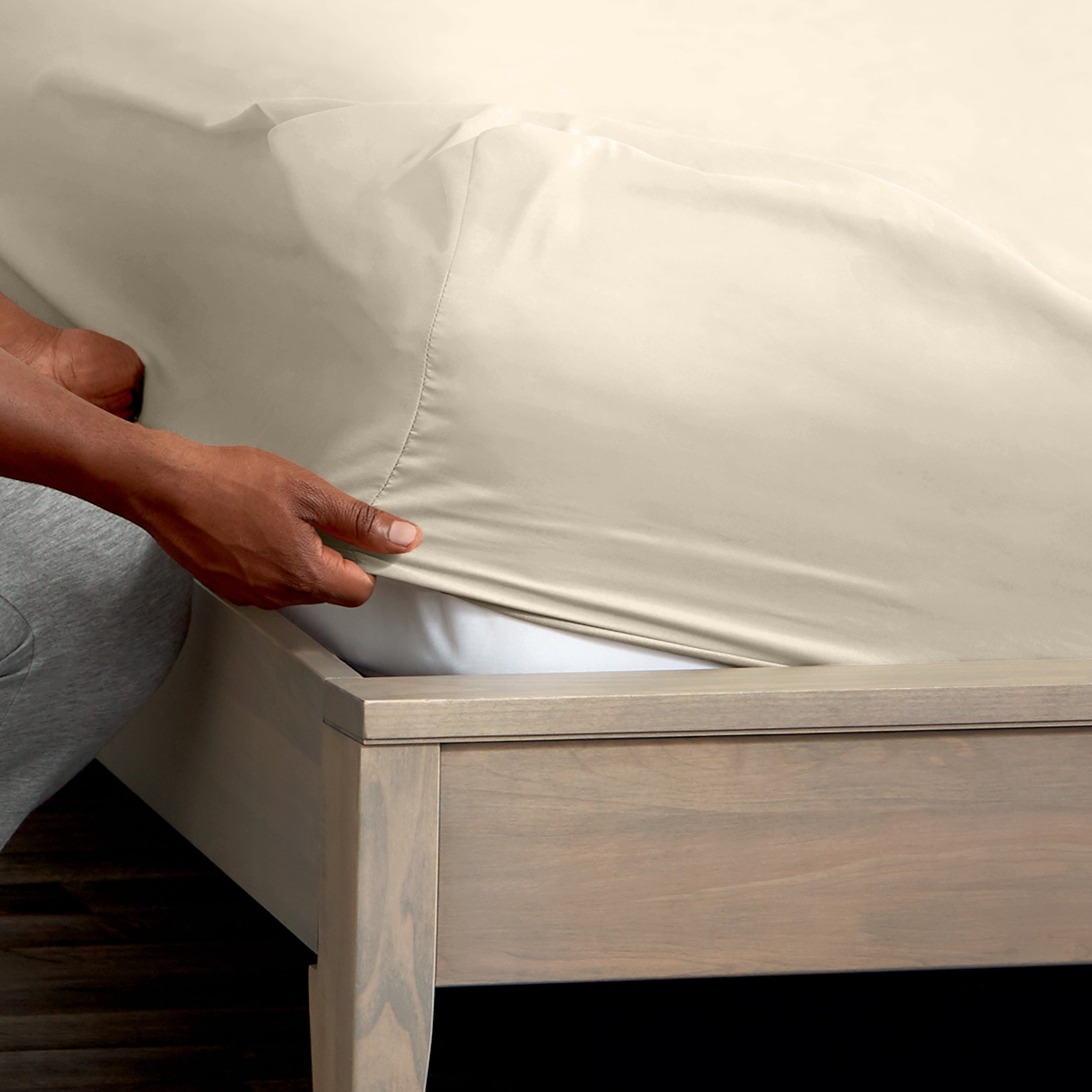 A man is putting a fitted sheet on a bed