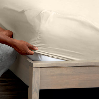 A man is putting a fitted sheet on a bed