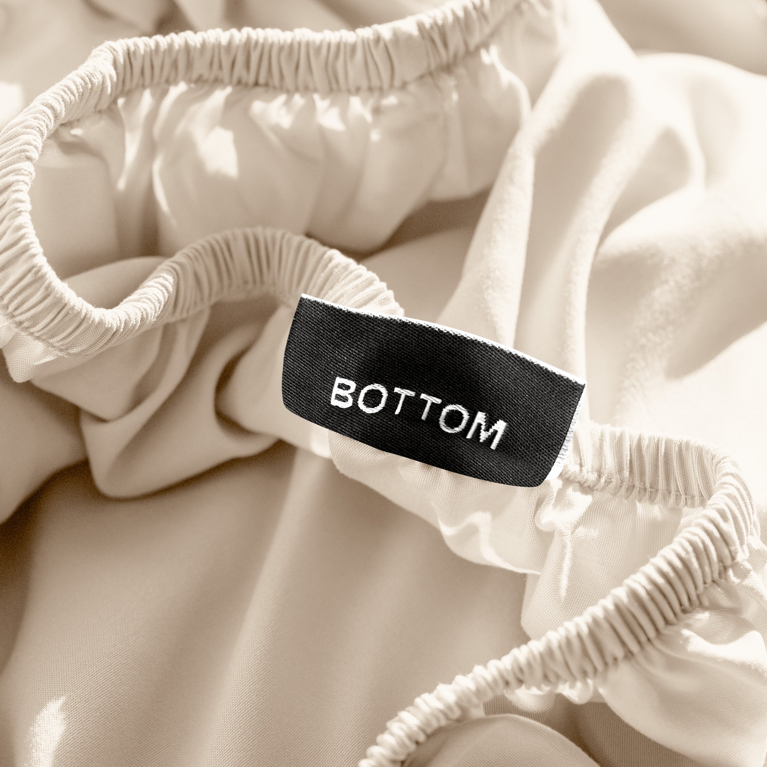 A close-up of a fitted sheet with a label printed with the word 'BOTTOM' in white.