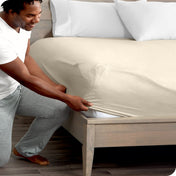 Man in white shirt and gray pants adjusting a fitted sheet on a bed.