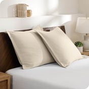 Two pillows with shams on a bed in a bedroom setting with a lamp and decor items.