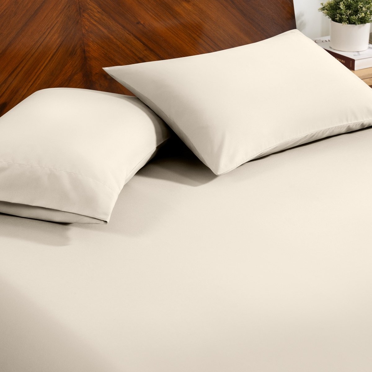 Fitted sheet and pillowcase set on a bed with a dark wood headboard and a small potted plant in the background.