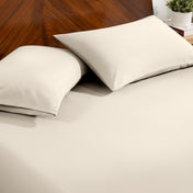 Fitted sheet and pillowcase set on a bed with a dark wood headboard and a small potted plant in the background.