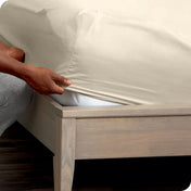 A man is putting a fitted sheet on a mattress