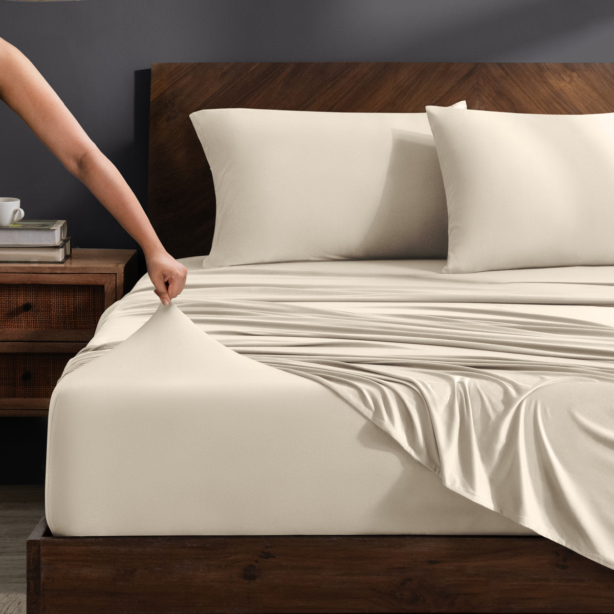 Person adjusting stretch sheets on a bed with a wooden headboard.